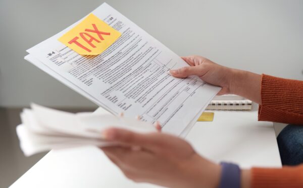 Tax filing. Individual holding tax documents and reviewing them at a desk. A person examines tax paperwork with a focus on accuracy and organization, preparing for tax submission.