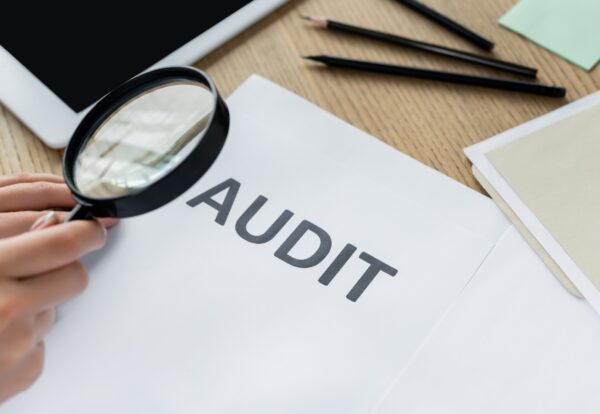Lupa examinando un documento de auditoría fiscal sobre un escritorio, simbolizando una auditoría del IRS a un negocio, revisión de impuestos y cumplimiento tributario empresarial.