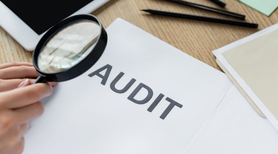 Lupa examinando un documento de auditoría fiscal sobre un escritorio, simbolizando una auditoría del IRS a un negocio, revisión de impuestos y cumplimiento tributario empresarial.