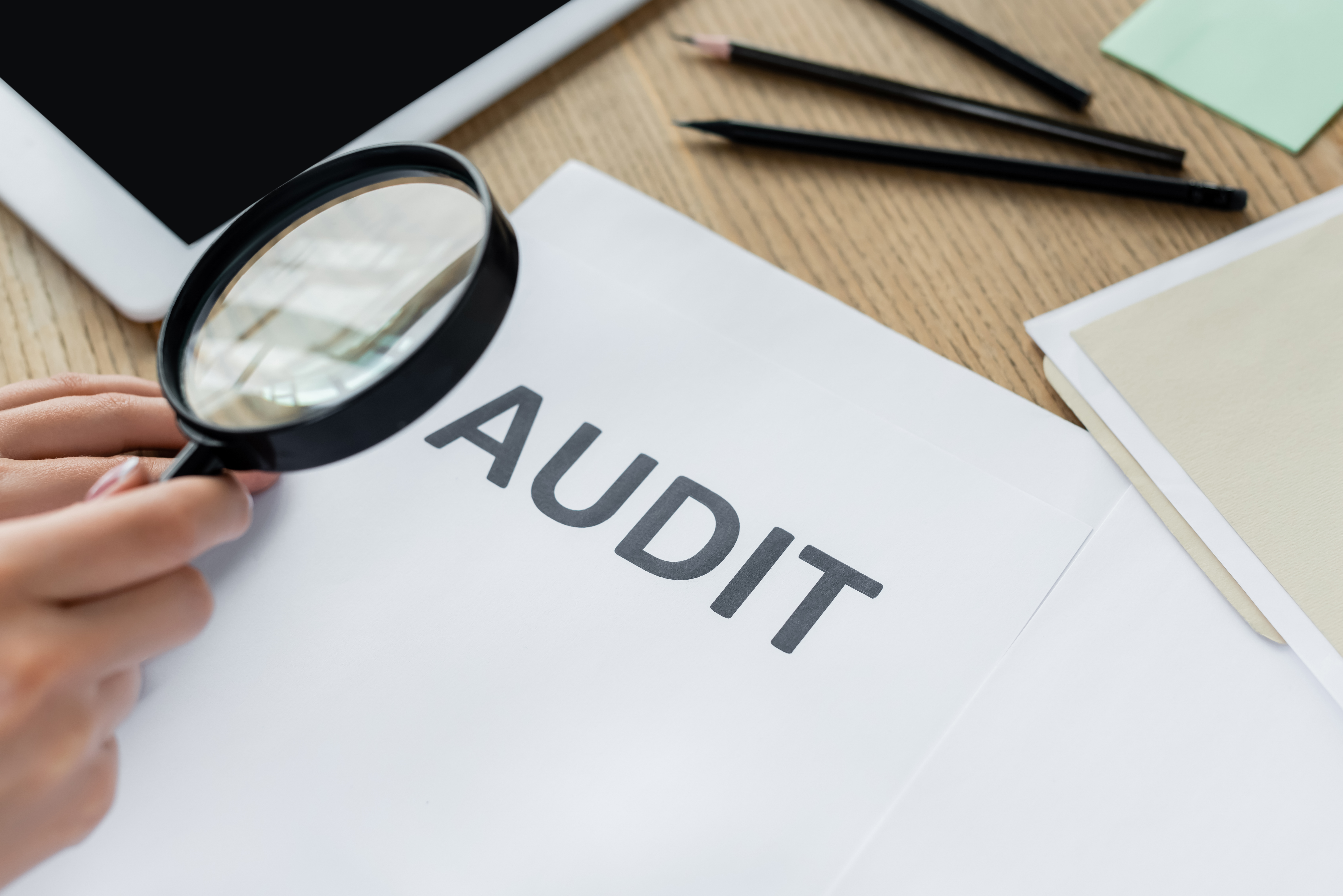 Lupa examinando un documento de auditoría fiscal sobre un escritorio, simbolizando una auditoría del IRS a un negocio, revisión de impuestos y cumplimiento tributario empresarial.